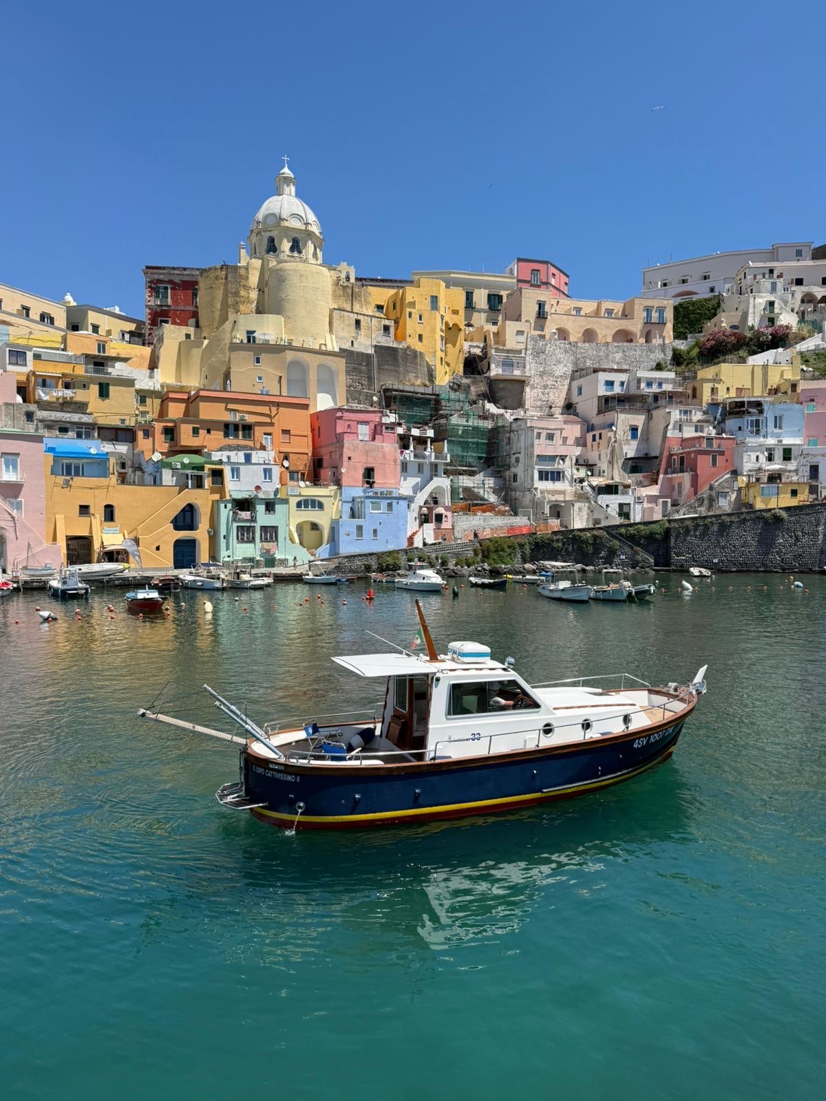 Side profile of the navy-blue Sciallino 33 gozzo inside Corricella harbour, church dome above