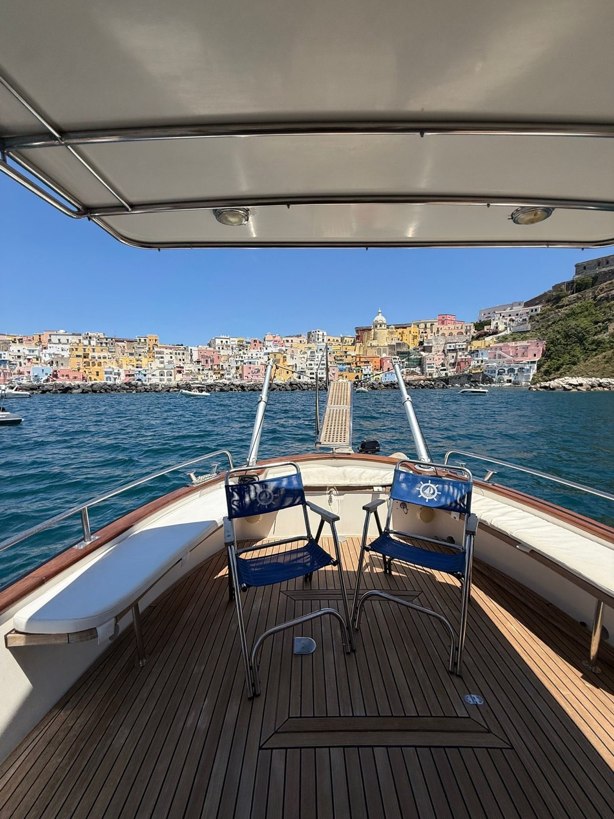 Teak cockpit with two blue deck chairs and gangway set towards Corricella, ready to welcome guests